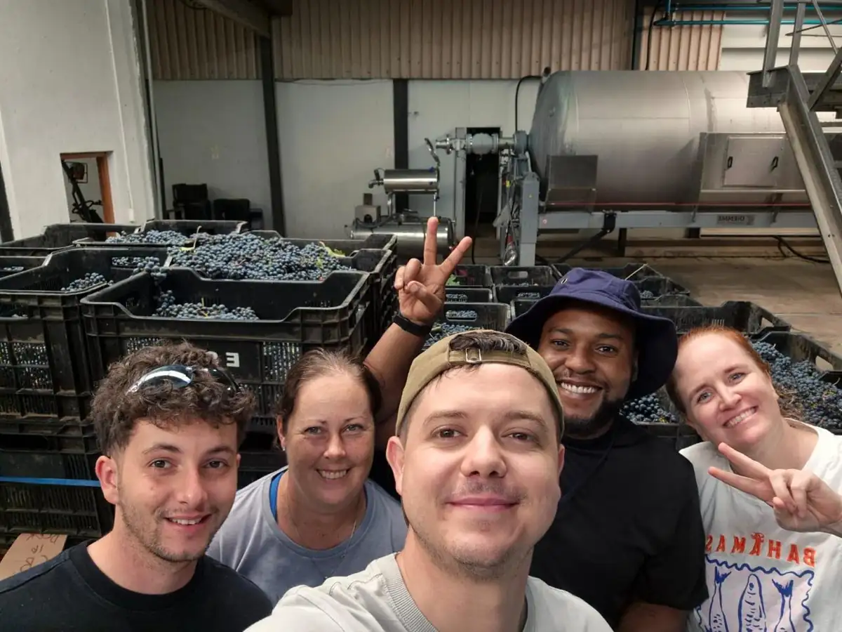 The group on the crush pad with crates of fruit and the press behind
