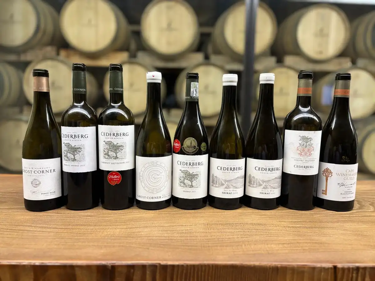 Nine bottles standing in a row on a wooden counter in front of stacked barrels