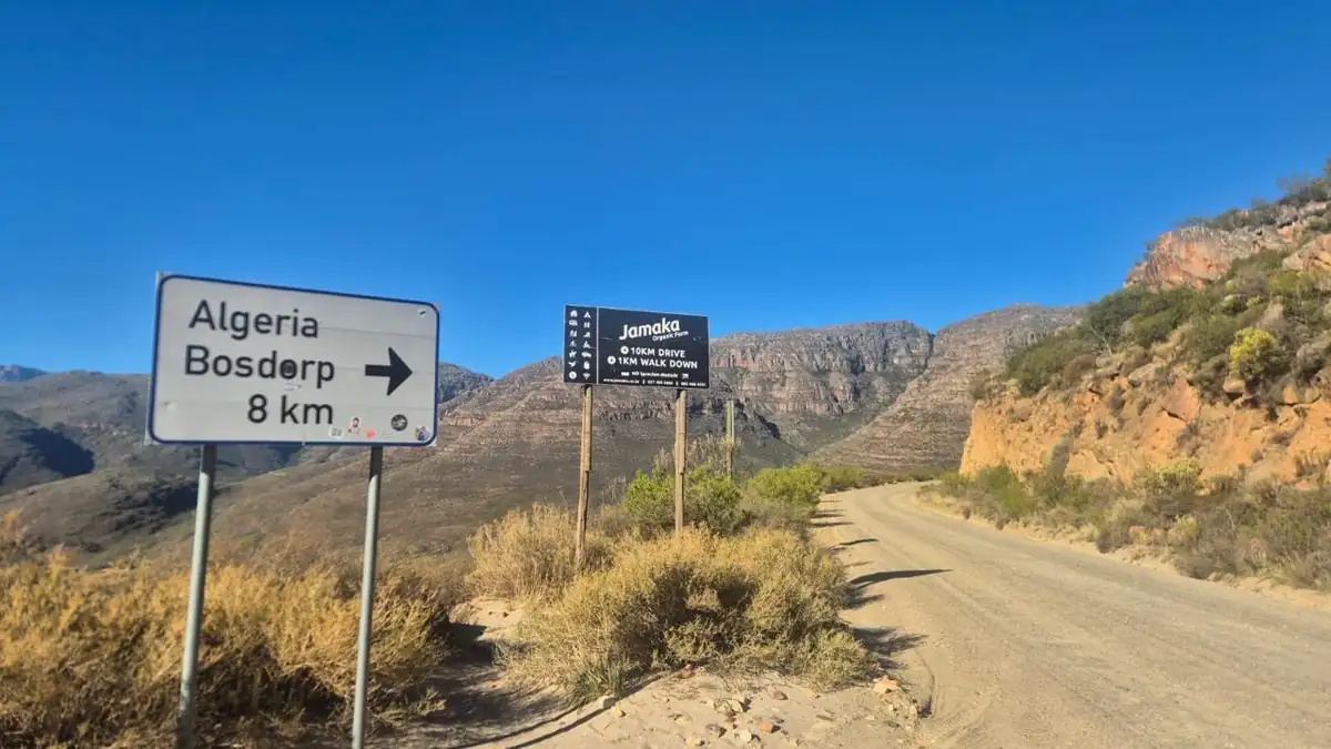 Signposts on a gravel road reading Algeria Bosdorp 8 km and Jamaka Organic Farm