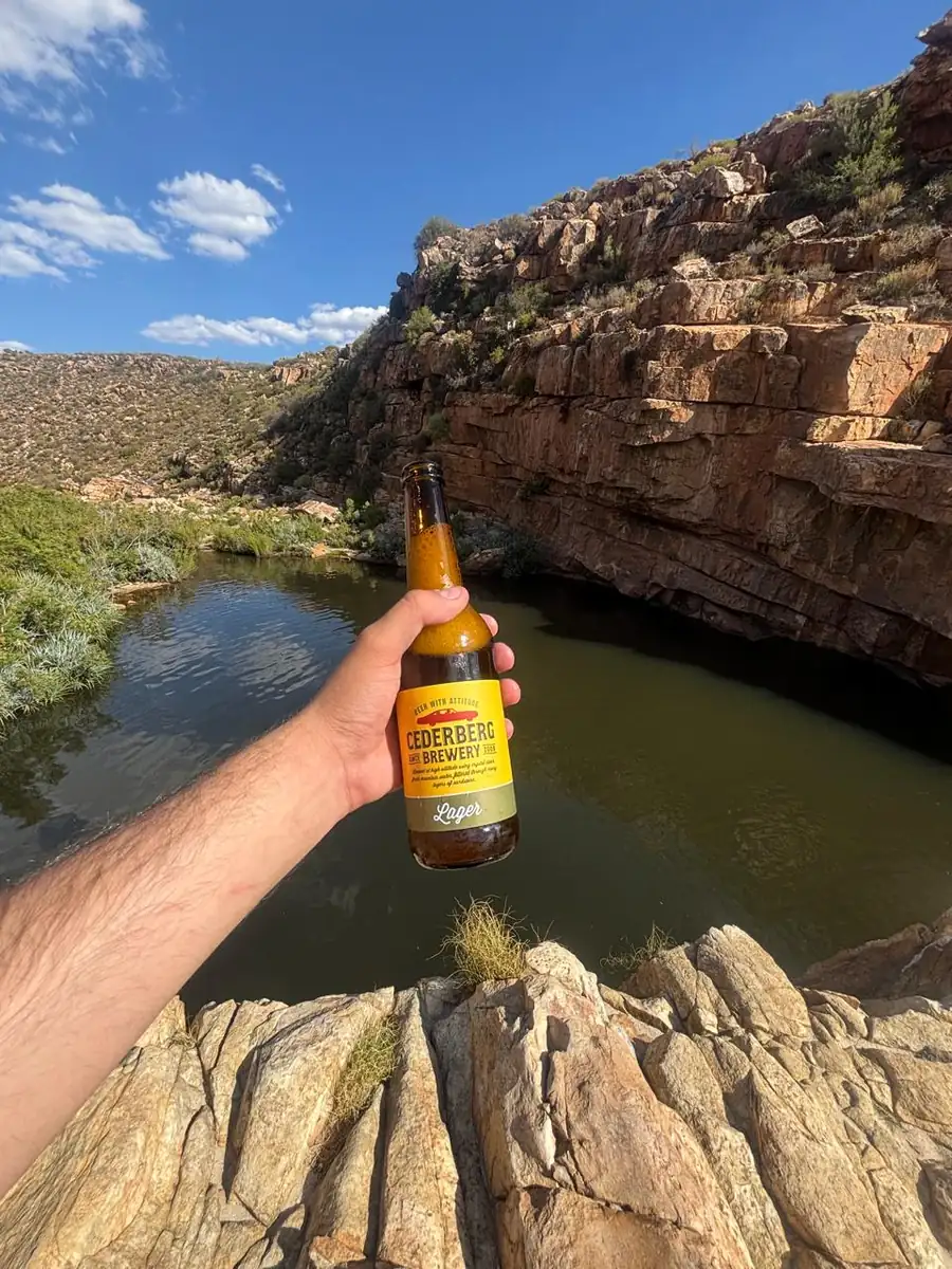 A bottle of Cederberg Brewery lager held up in front of a rock pool